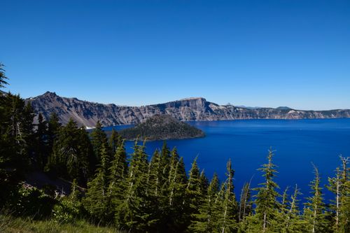 Free Vast panoramic view of Crater Lake with clear sky and lush forest in Oregon's Crater Lake National Park. Stock Photo