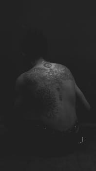 Artistic grayscale image featuring intricate tattoos on a man's back.