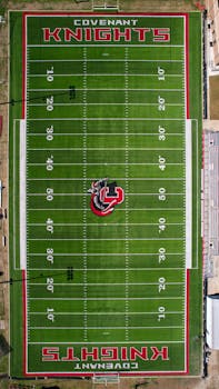 A top-down aerial view of a green football field marked 'Covenant Knights' with clear yard lines.