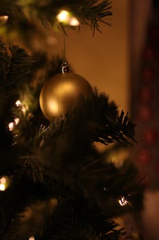 Close-up of a golden ornament hanging on a Christmas tree with soft lighting.