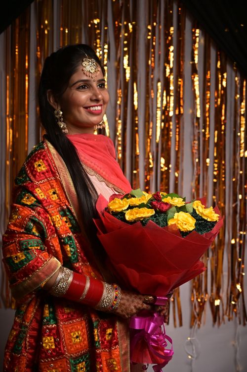 Free A woman in vibrant traditional attire holds a bouquet of yellow flowers, smiling gracefully. Stock Photo