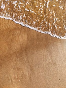 Close-up of golden sand and foamy ocean waves at a secluded beach.