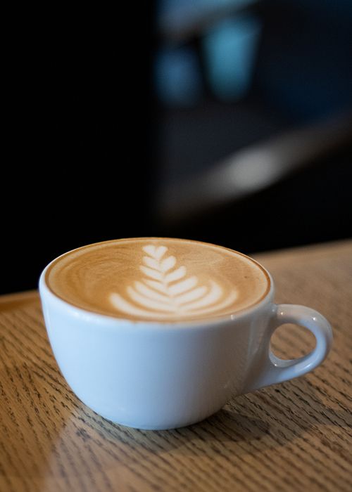 Free Close-up of a creamy latte with latte art served in a white cup on a wooden table. Stock Photo