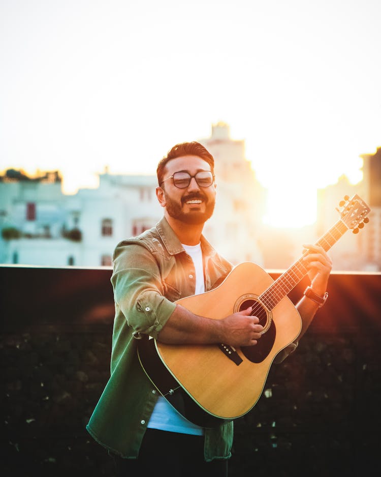 Bearded Man Wearing Sunglasses While Playing Acoustic Guitar During Sunset