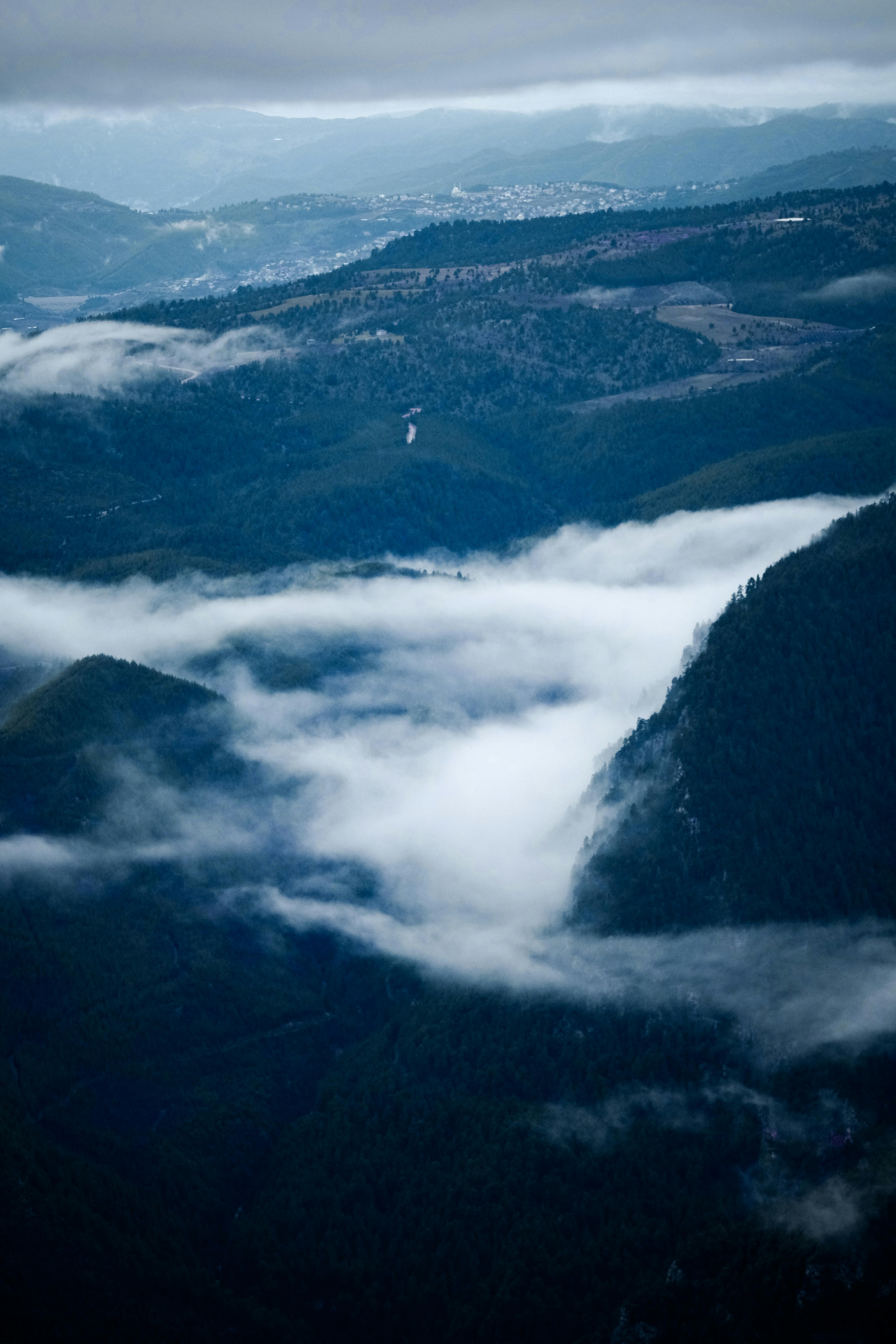 A stunning aerial view showcasing fog and clouds enveloping majestic mountains.