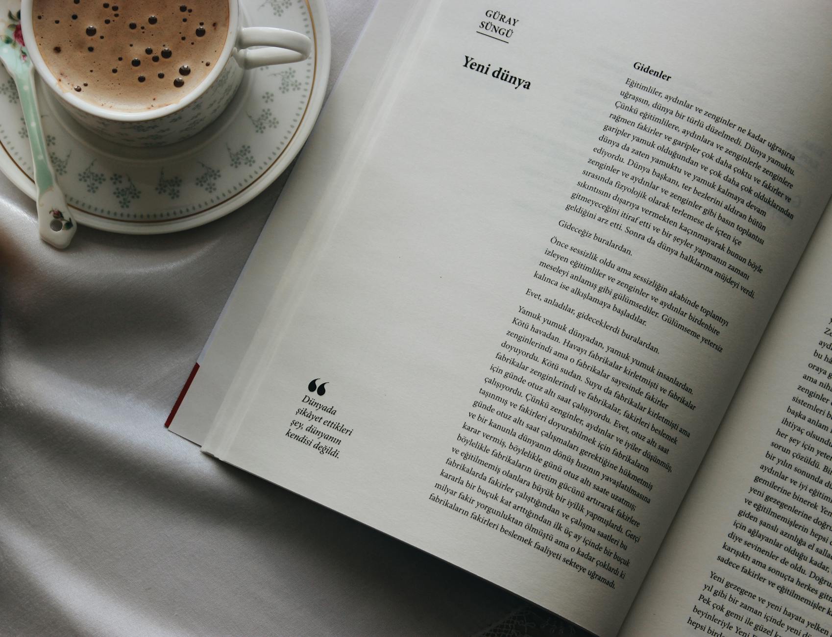 Cup of Turkish coffee next to an open book on a linen bedsheet.