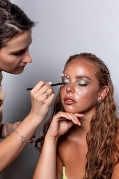 Makeup artist applying green eye shadow to model in studio photoshoot.