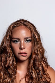 Studio headshot of a young woman with curly red hair on a white background.