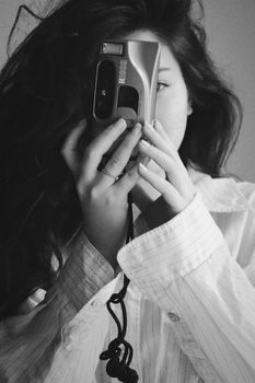 Black and white photo of a woman covering her face with a vintage camera.