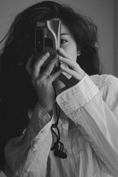 Woman capturing a self-portrait in grayscale using a vintage camera indoors.