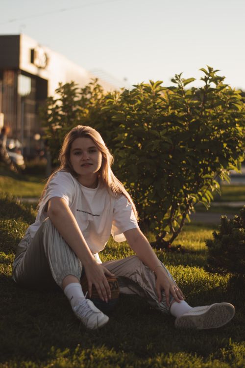 Free Woman in casual attire sitting on a grassy park lawn during sunset. Stock Photo