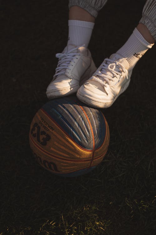 Free A Person Wearing White Rubber Shoes Stepping on a Sports Ball Stock Photo
