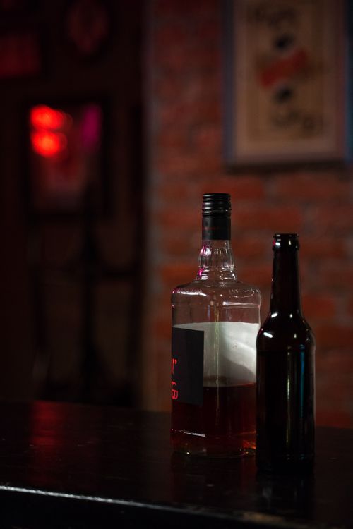 Free A dimly lit bar setting featuring a whiskey bottle and a beer bottle on a counter. Stock Photo