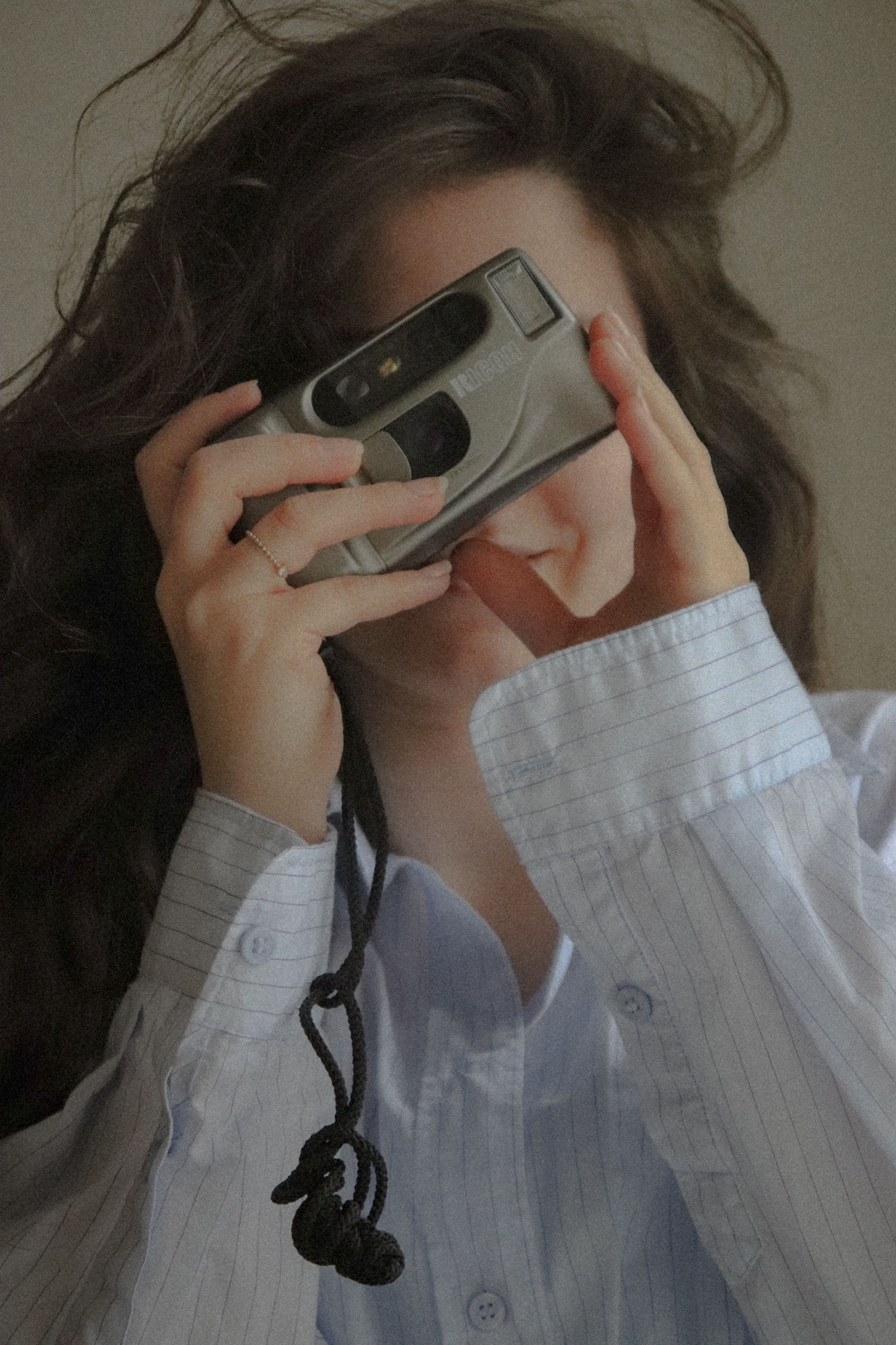 A woman in a striped shirt taking a photo with a vintage camera indoors.