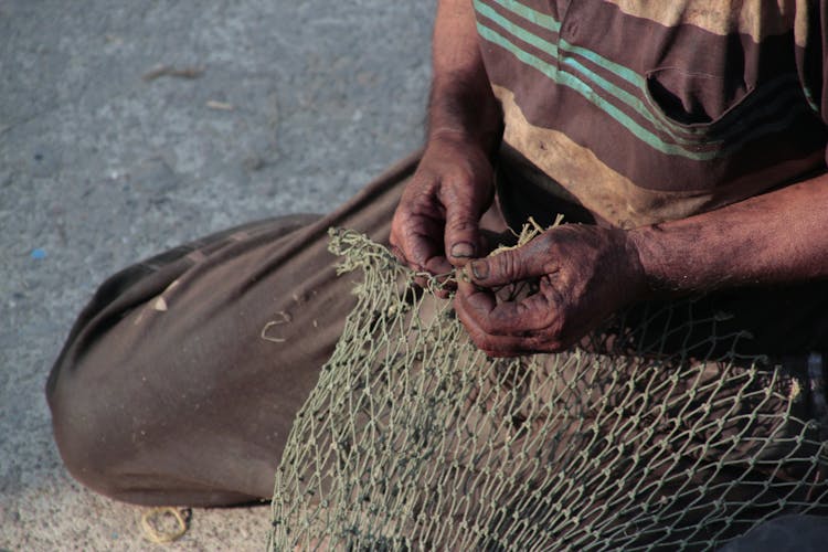 Man Kneeling On Ground And Making Fishing Net