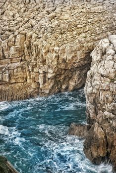 High-angle view of eroded rocky coastline with crashing waves in Cantabria, Spain.