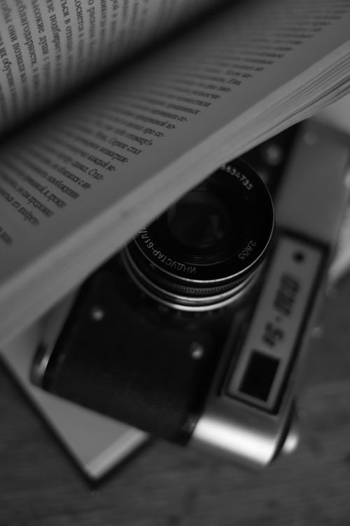 Free Black and white close-up of a vintage film camera peeking through an open book. Stock Photo