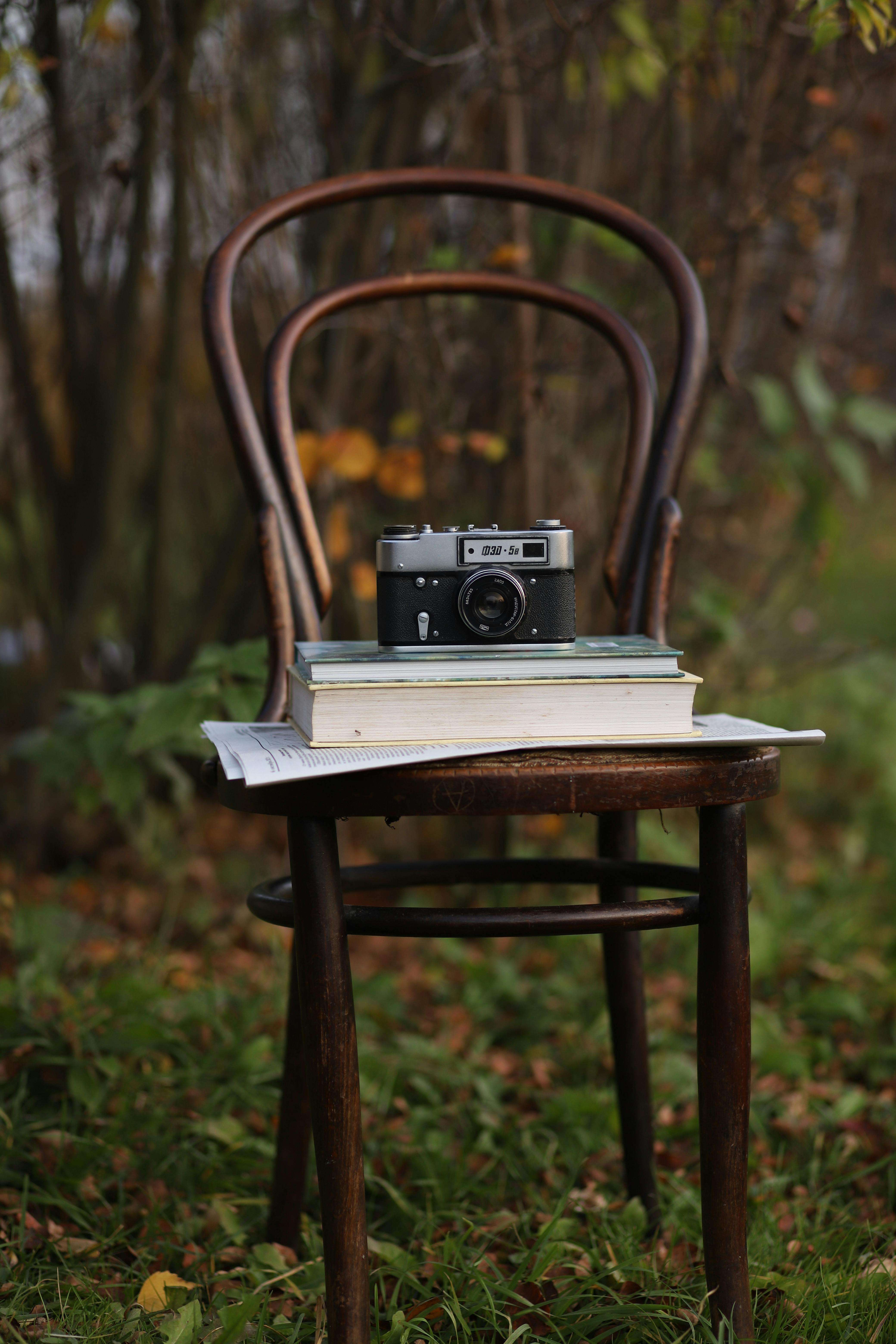 Film camera on books atop a wooden chair in an outdoor setting, evoking nostalgia.