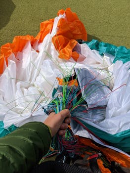 A close-up of colorful parachute lines being held by a human hand on a sunny day, featuring vibrant colors and textures.
