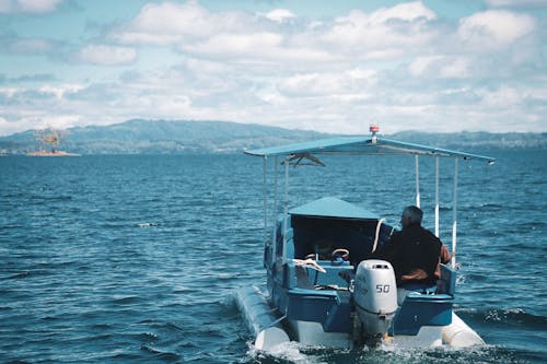 Photo of a Man in a Brown Jacket Riding a Motor Boat