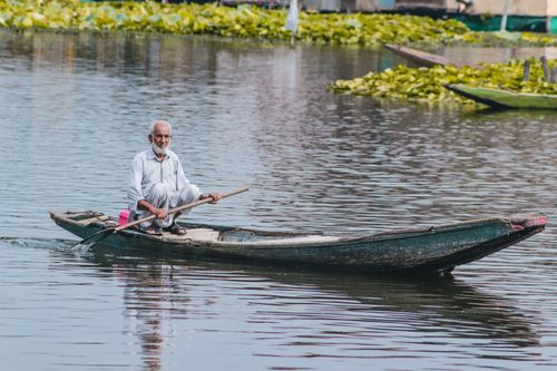 Free An elderly man paddling a canoe on a serene lake, surrounded by lush greenery. Stock Photo