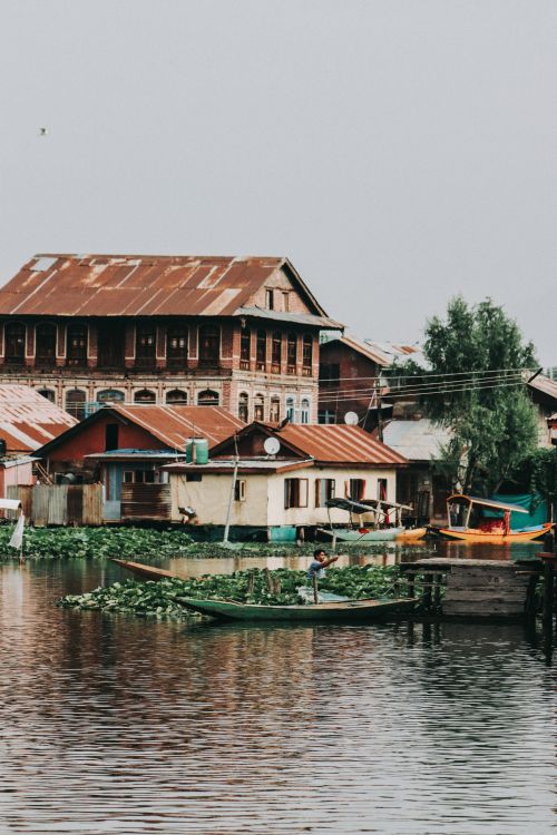 Free Picturesque scene of a rustic floating market with vibrant boats and traditional architecture on a calm river. Stock Photo