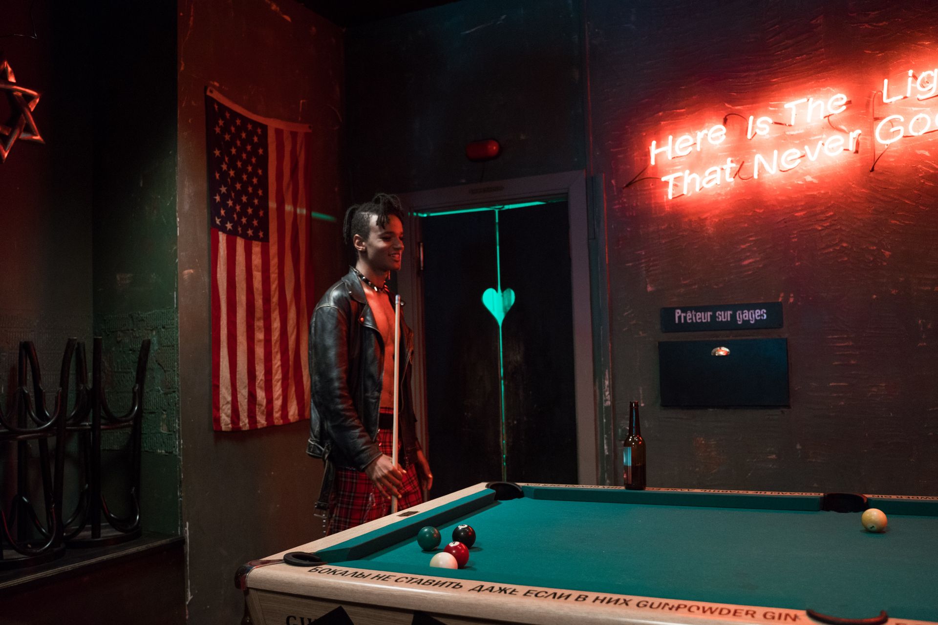 Man in black leather jacket at a billiards table under vibrant neon lights.