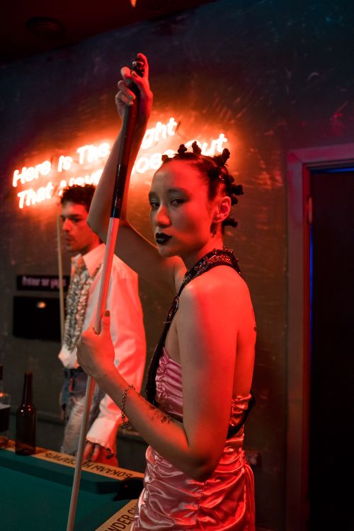 Free A fashionable woman holding a cue stick in a neon-lit room while playing billiards. Trendy and modern atmosphere. Stock Photo