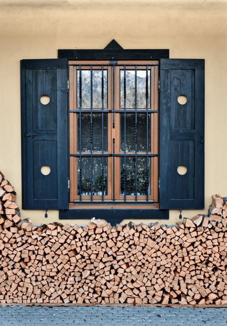 Cozy exterior design featuring a rustic window with neatly stacked firewood against a concrete wall.