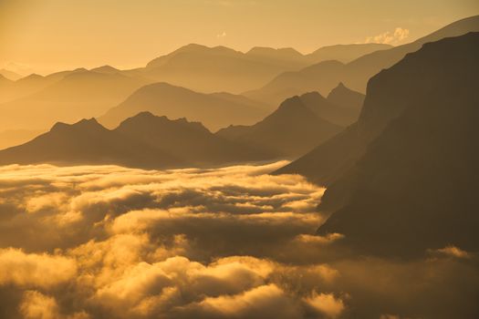 Breathtaking view of mountain peaks surrounded by clouds at sunrise, creating a golden hue.