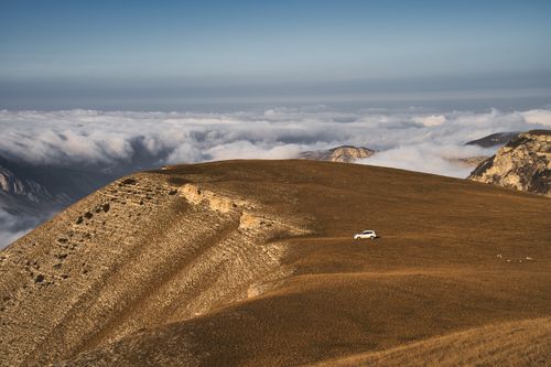 Free A solitary car travels along a mountain ridge enveloped by scenic clouds and rugged terrain. Stock Photo