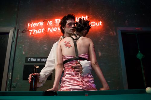 Free A couple embraces romantically in front of a neon sign at a billiard table in a dimly lit room. Stock Photo