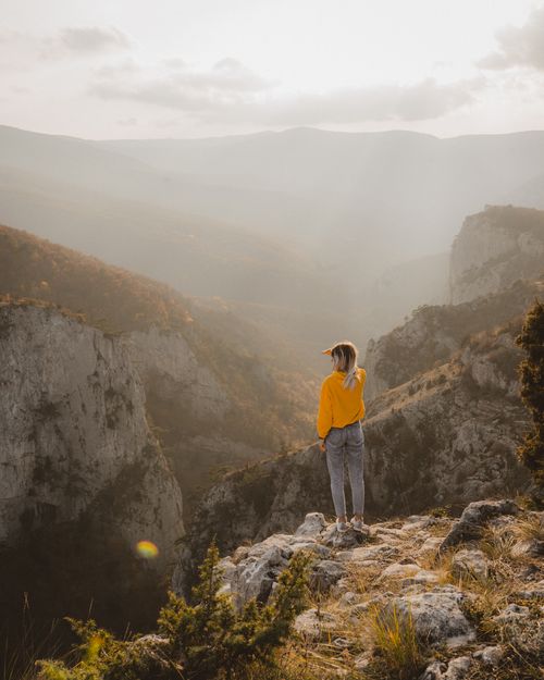 Free Woman views majestic foggy landscape from cliff. Captivating adventure scene. Stock Photo