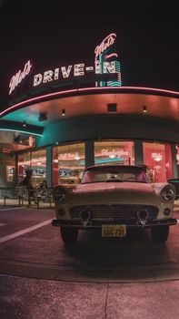 Vintage car parked at a neon-lit drive-in diner, evoking nostalgia and retro vibes.