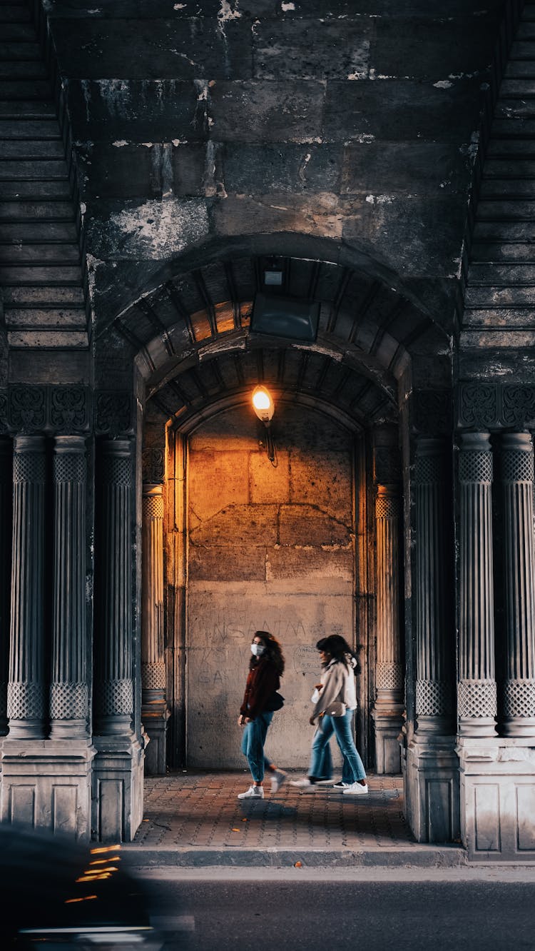 Girls Walking On Sidewalk Under Arcades