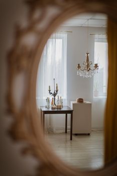 Reflective view of an elegant room through a mirror, featuring a chandelier and a table setup.