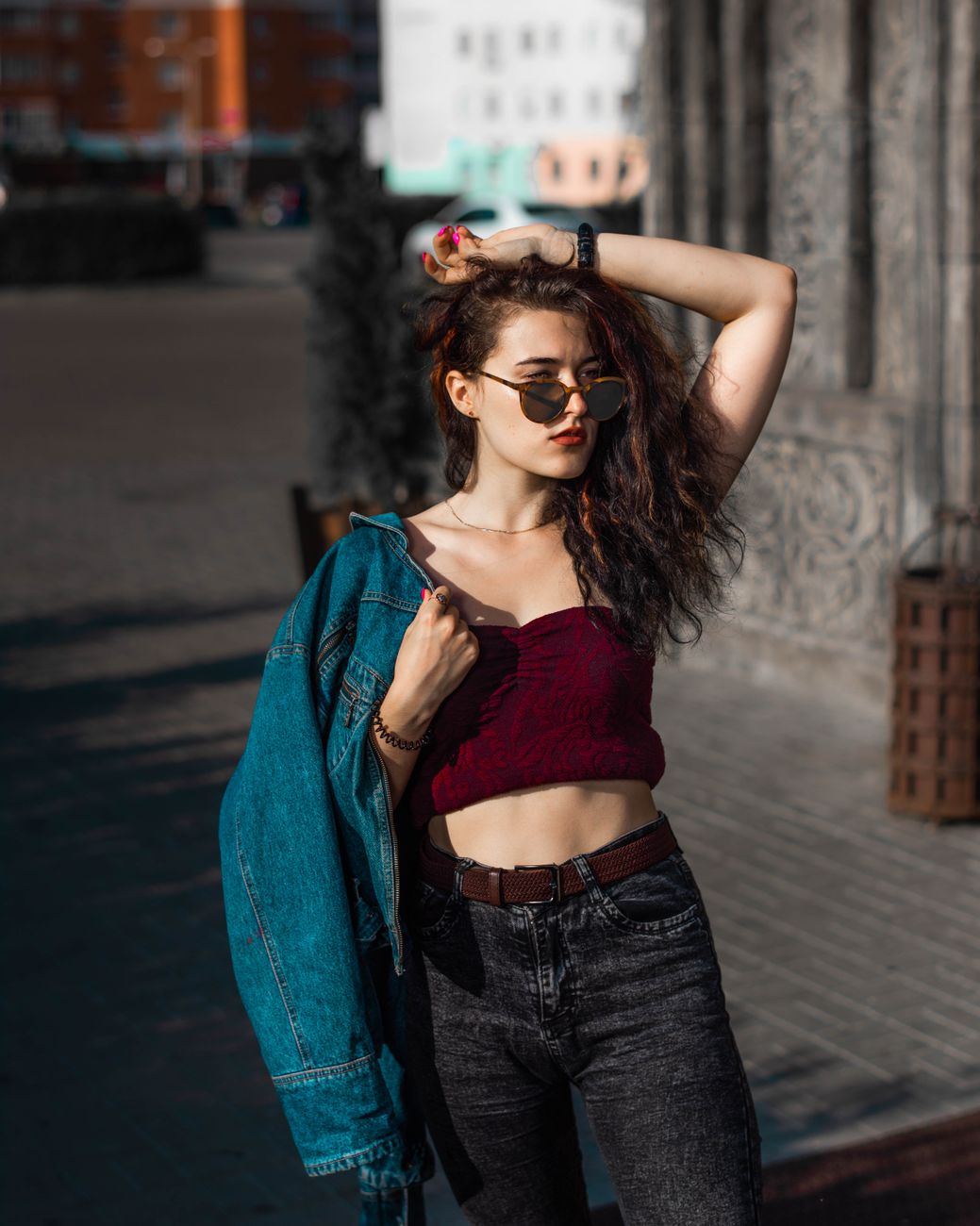 Trendy woman in casual outfit with sunglasses posing on a city street under sunlight.