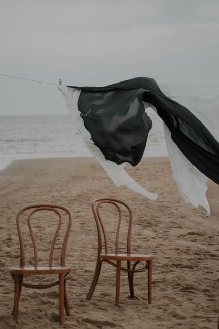 Two wooden chairs with laundry hanging on a sandy beach under a cloudy sky.