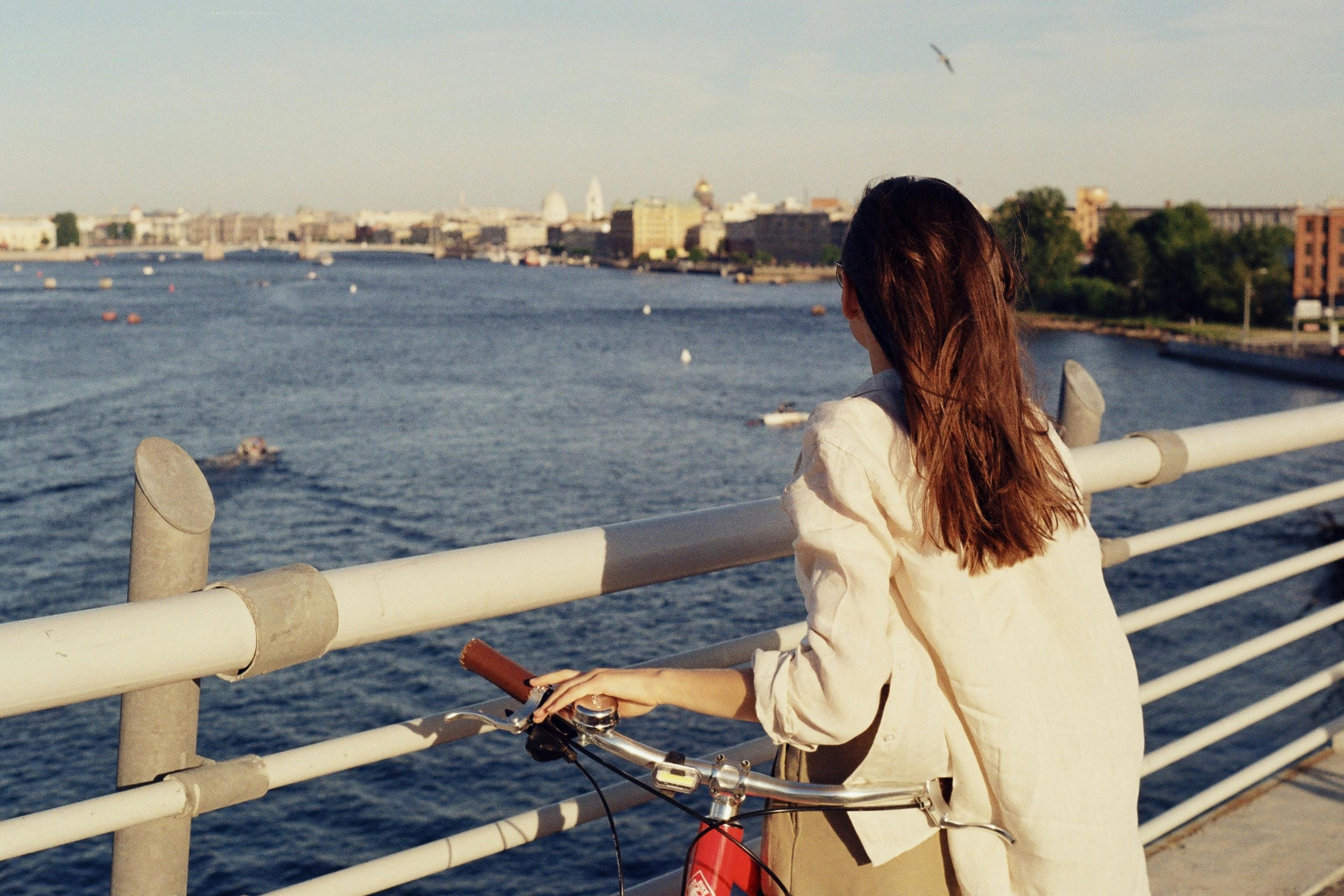 A woman with a bike gazes over the river in Saint Petersburg, Russia, on a sunny day.