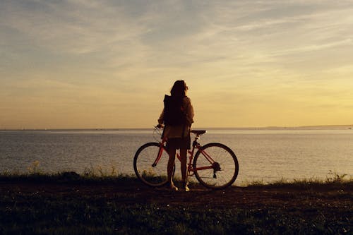 Woman Holding a Bicycle while Standing Near Water