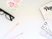 时尚的扁平工作空间必需品包括粉红玫瑰、杂志和眼镜