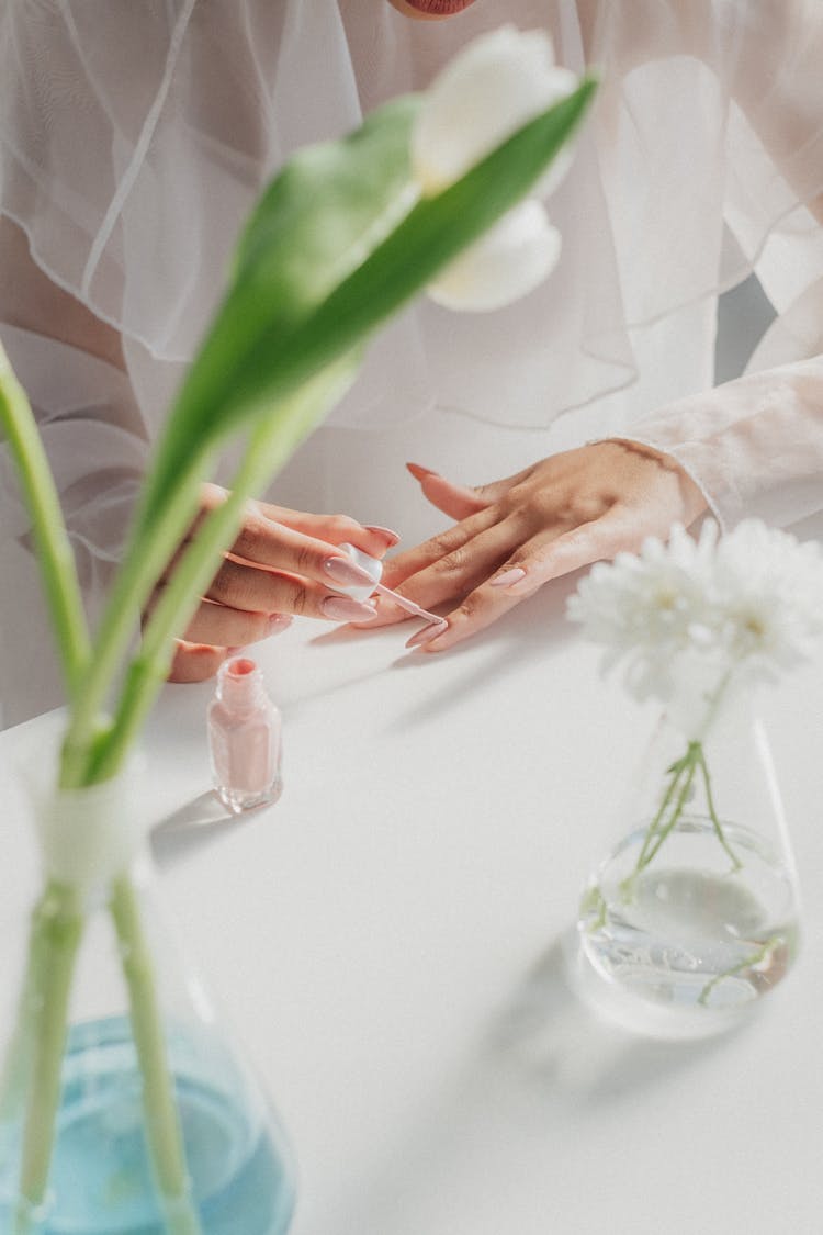 Woman Painting Nails With Flowers In Glass Flasks In Foreground