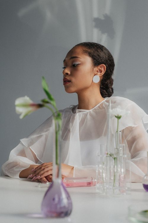 Free A contemplative woman seated at a table with botanical flasks in a minimalist setting. Stock Photo