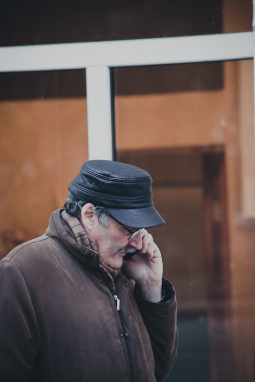Free Senior man wearing a leather hat and coat, talking on the phone outdoors. Stock Photo