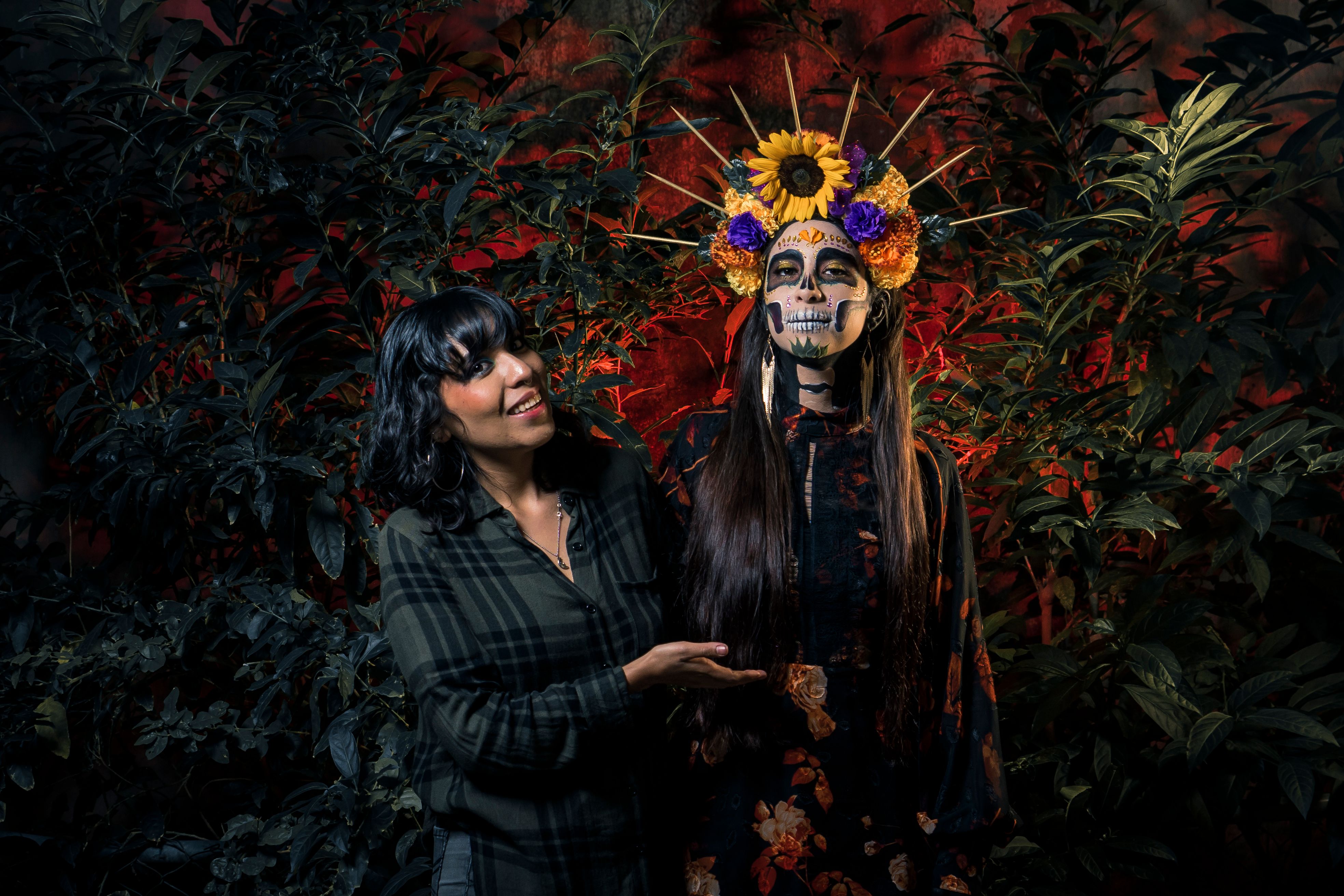 Two women in traditional Día de los Muertos attire with colorful floral headdresses.