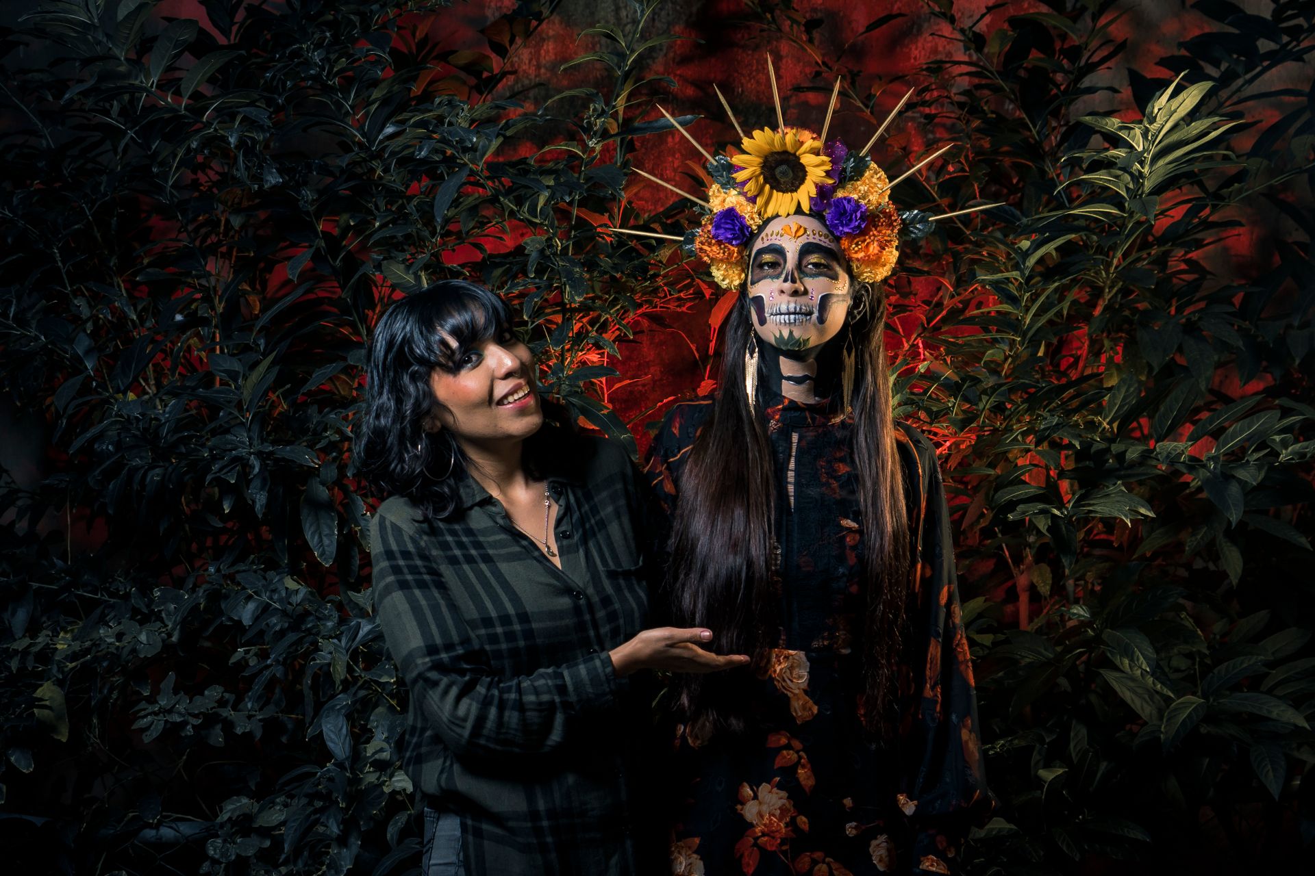 Two women in traditional Día de los Muertos attire with colorful floral headdresses.