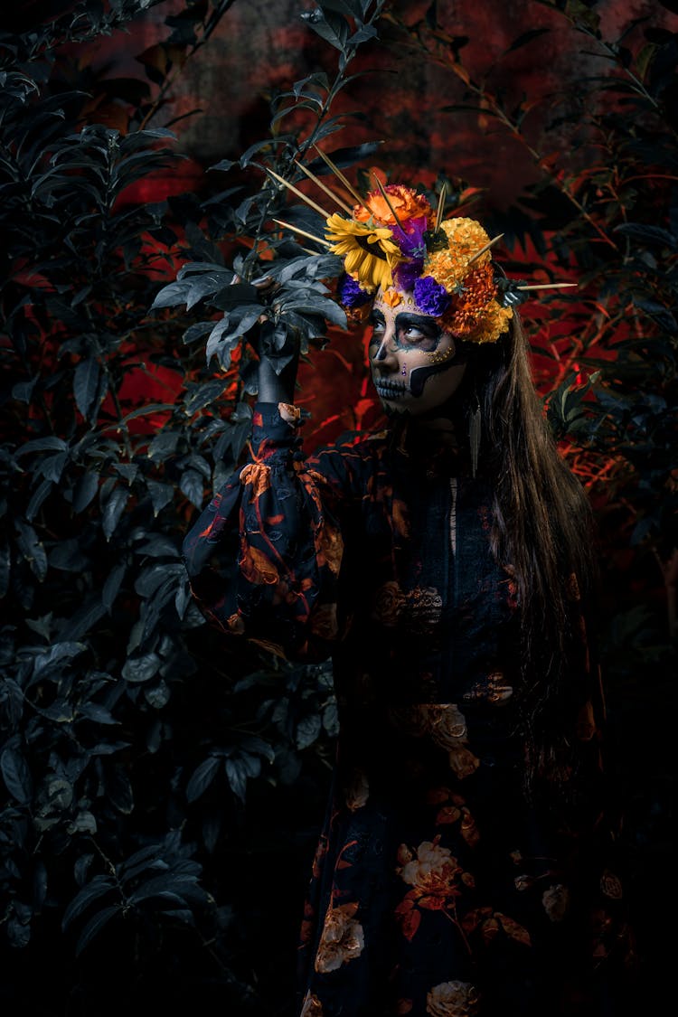 A Woman With Painted Face Wearing A Floral Headdress Looking At The Leaves Of A Plant