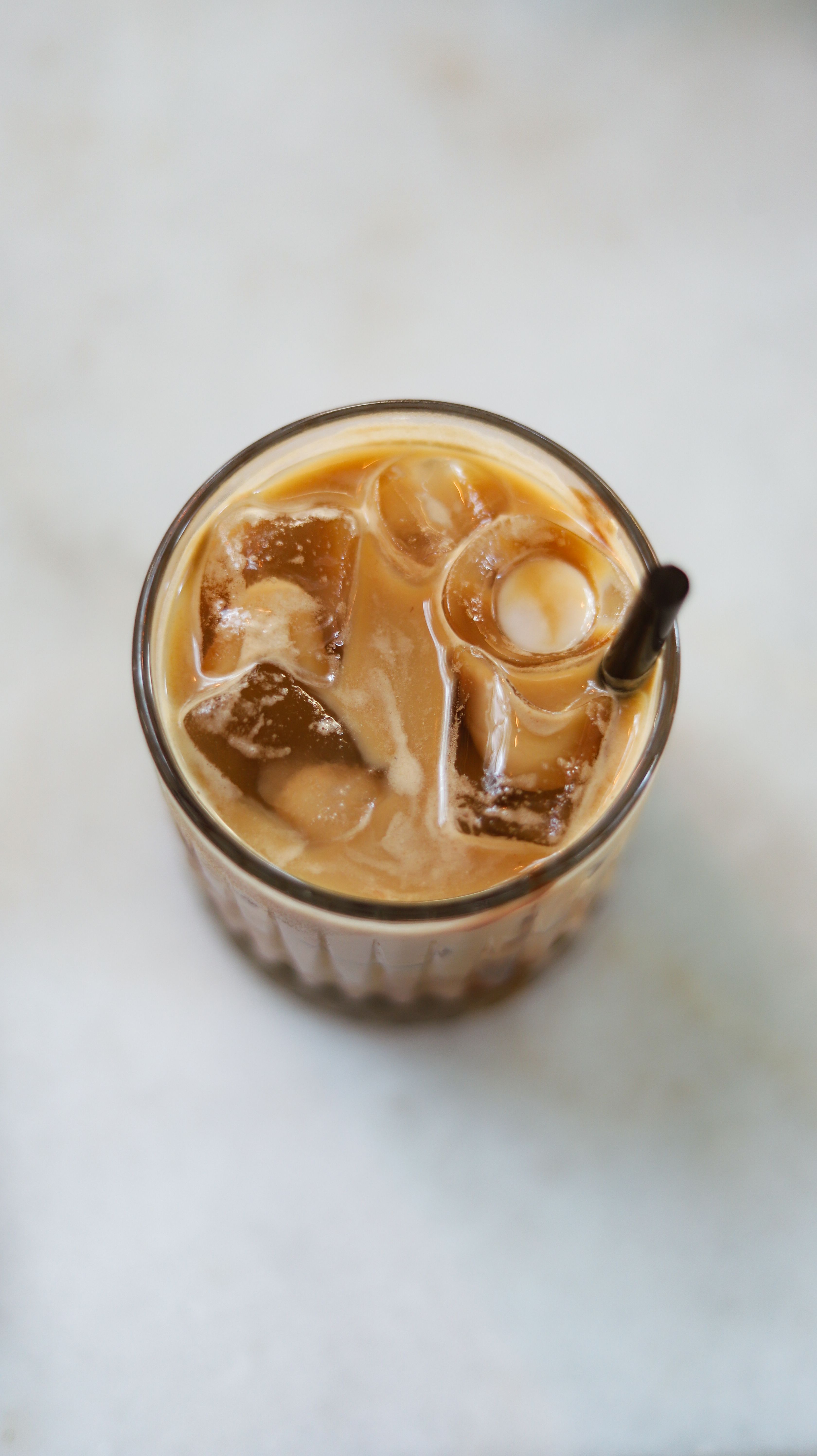 Top view of iced coffee with ice cubes and straw in a glass on a white background.