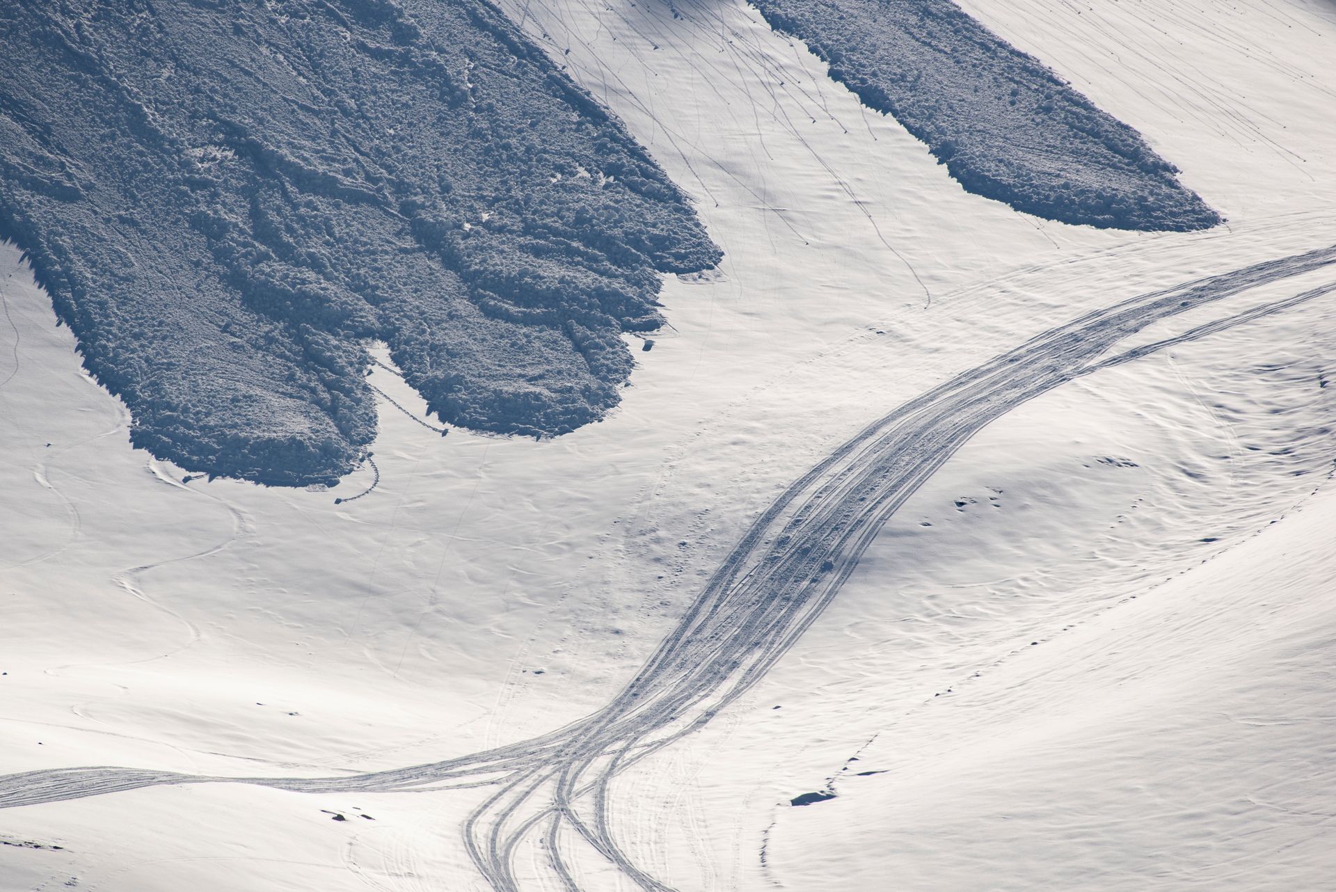 Aerial view of snowy Icelandic terrain with vehicle tracks and rugged slopes.