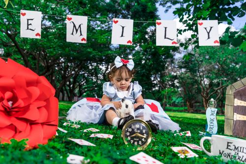 Free A child in Alice costume sits with a rabbit in a whimsical garden setting, surrounded by themed decorations. Stock Photo